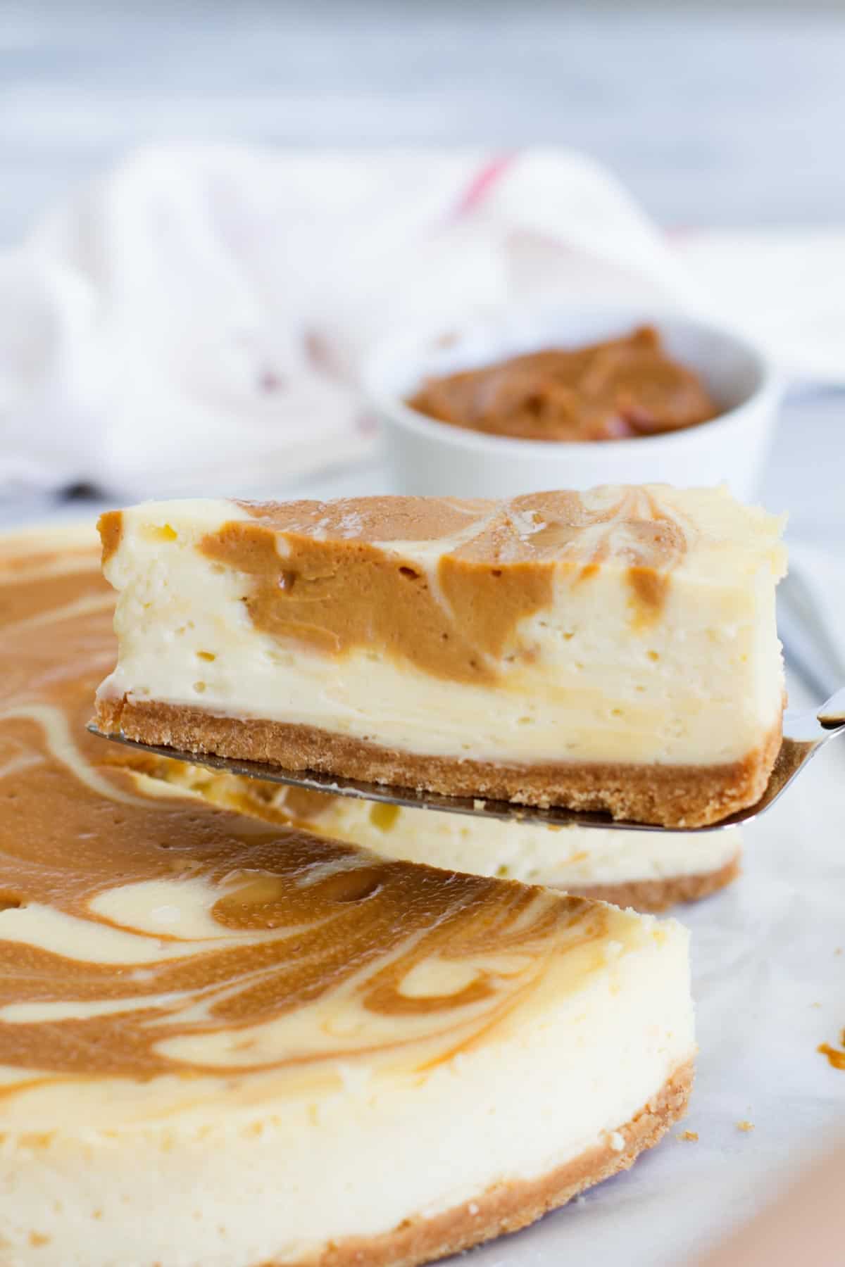 slice of dulce de leche cheesecake being taken from the full cheesecake.