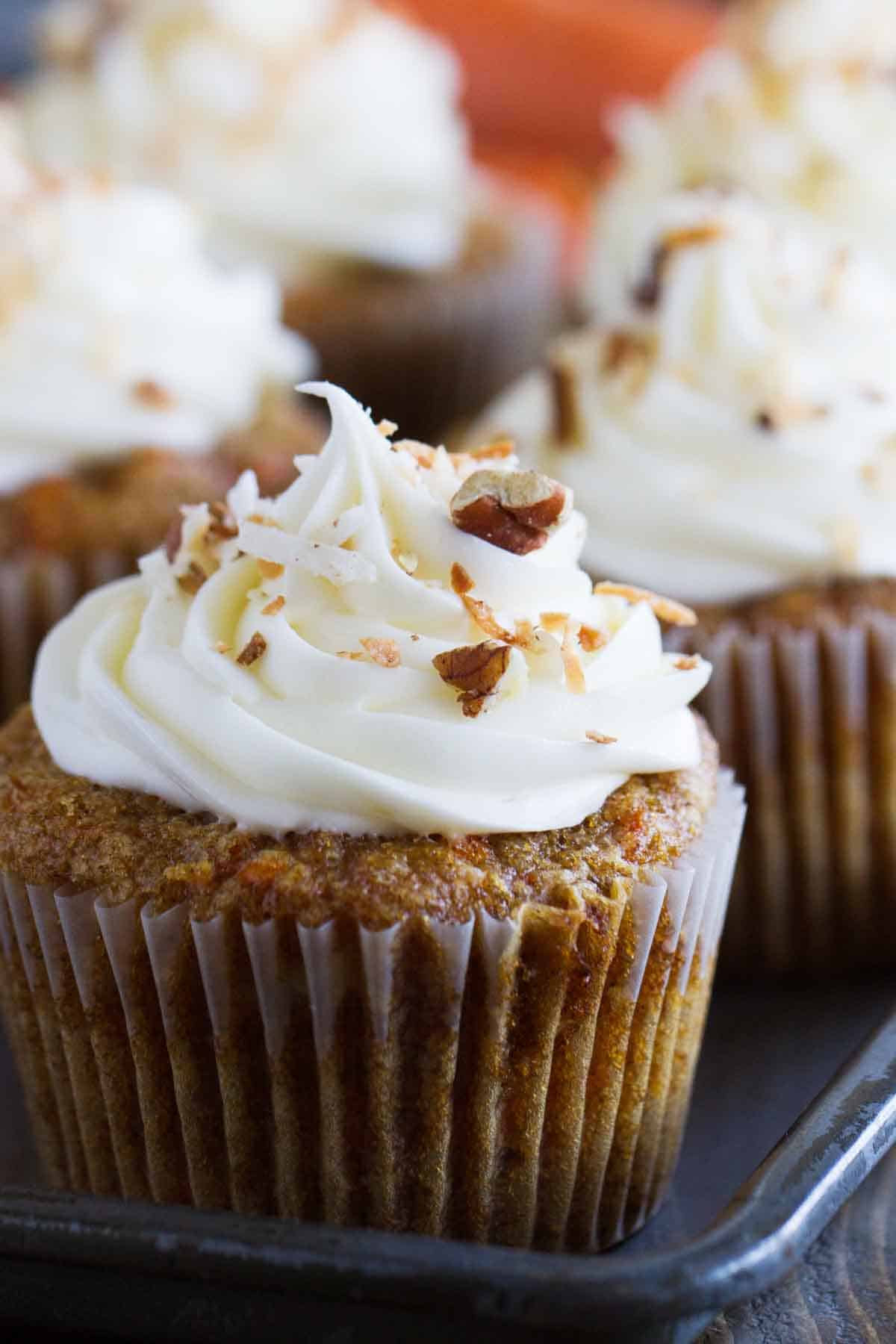 close up of carrot cake cupcake topped with cream cheese frosting, nuts, and coconut