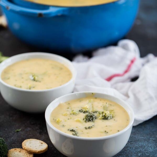 two bowls of broccoli cheese soup with a pot in the back