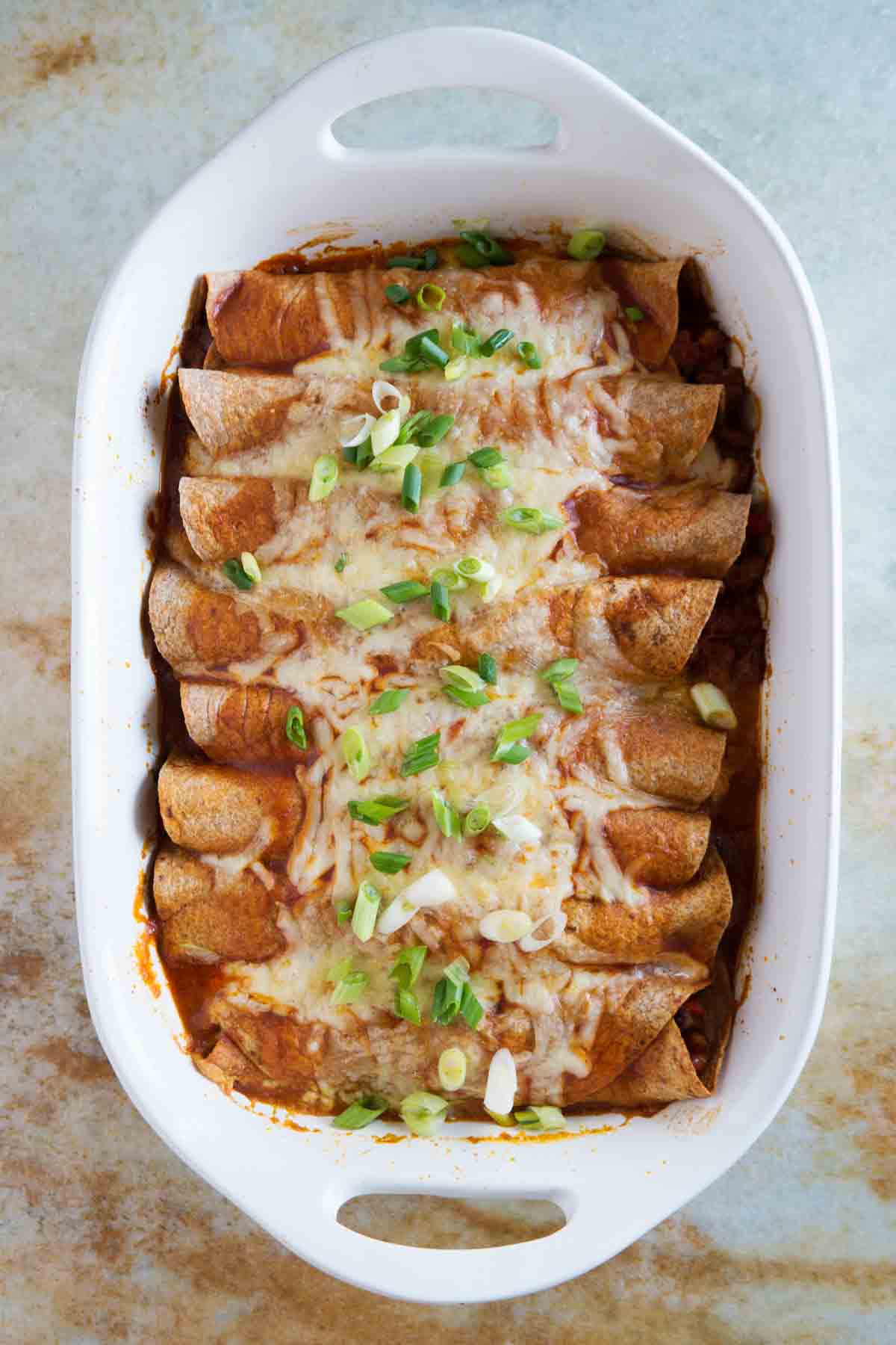 White casserole dish filled with Sausage and Bean Enchiladas.