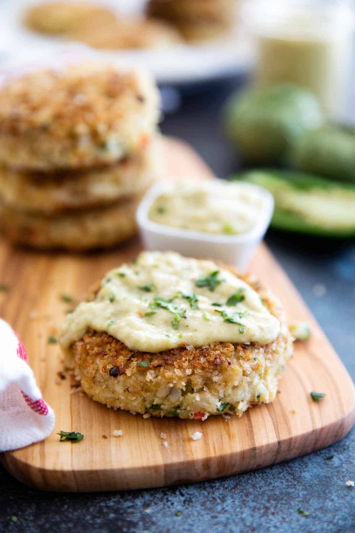 Green Chile Crab Cakes topped with Tomatillo Salsa with stack of crab cakes behind.