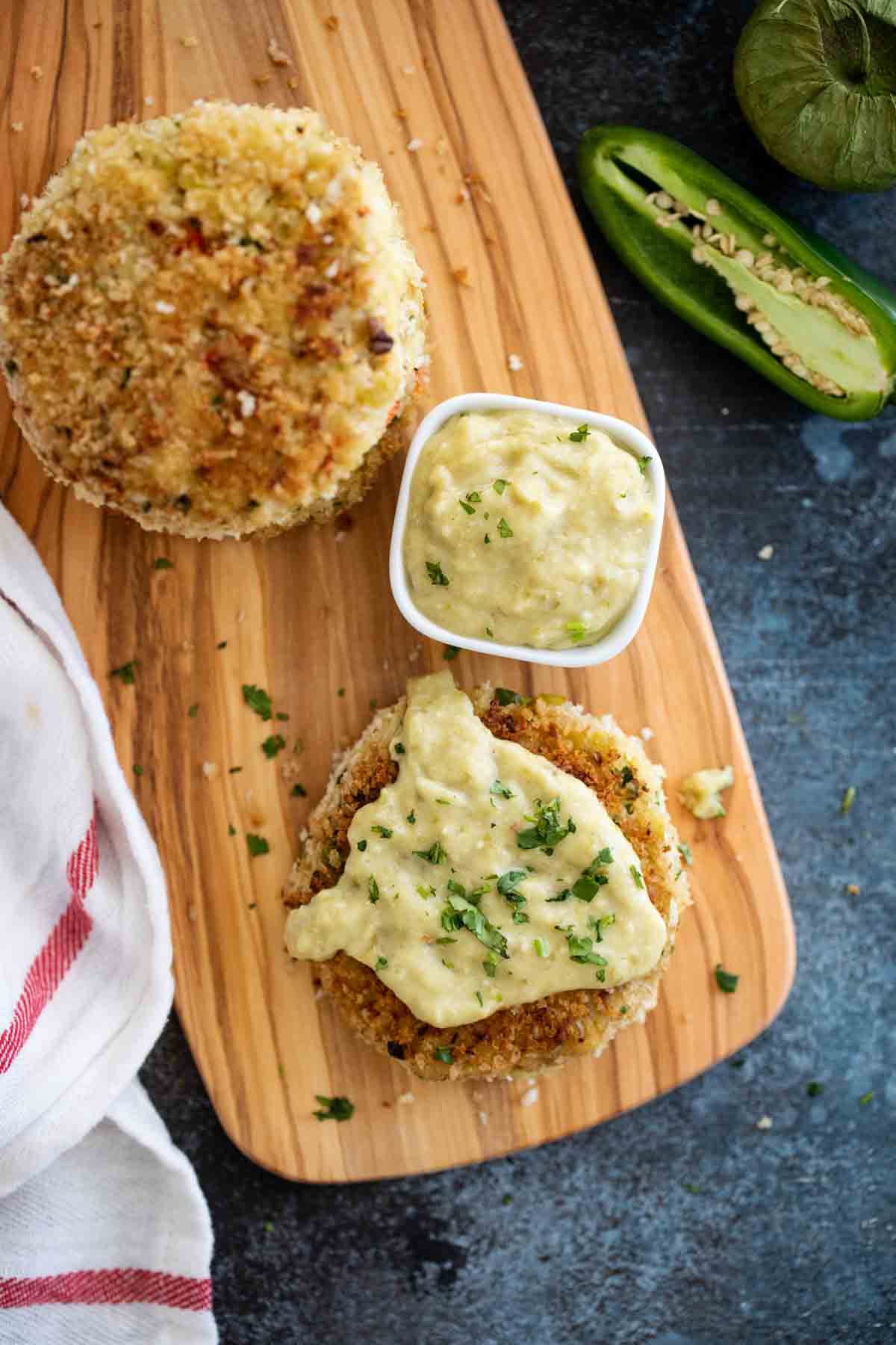 Green chile crab cake topped with tomatillo salsa on a wooden board.