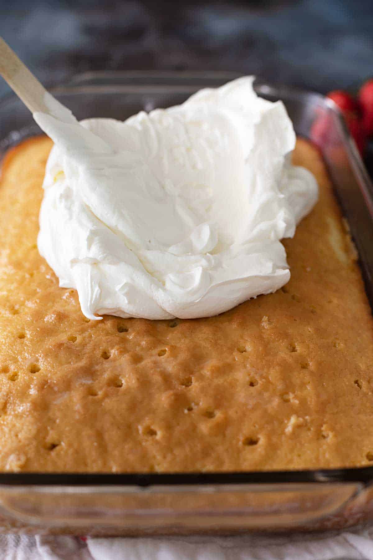 spreading whipped cream on top of tres leches cake