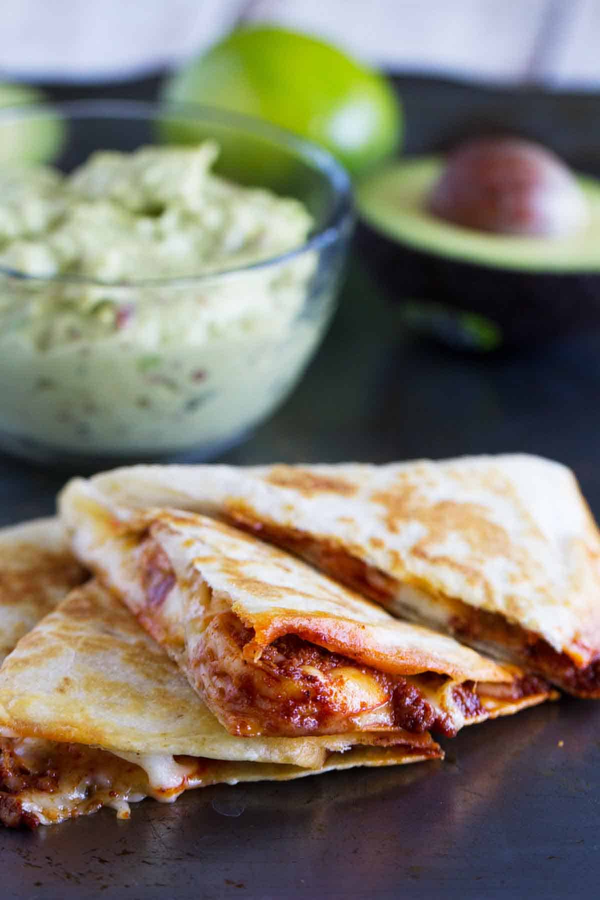 Shrimp Quesadilla with chorizo and cheese with a bowl of smoky guacamole in the background.