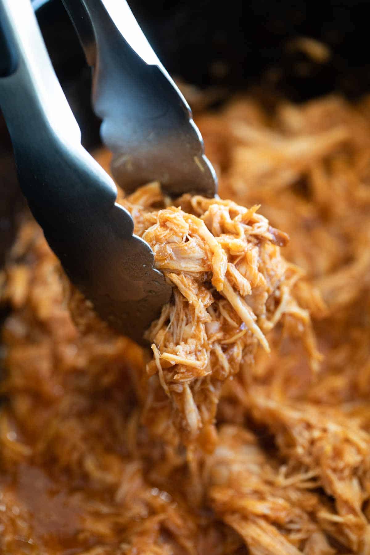 Slow cooker pulled chicken in tongs.