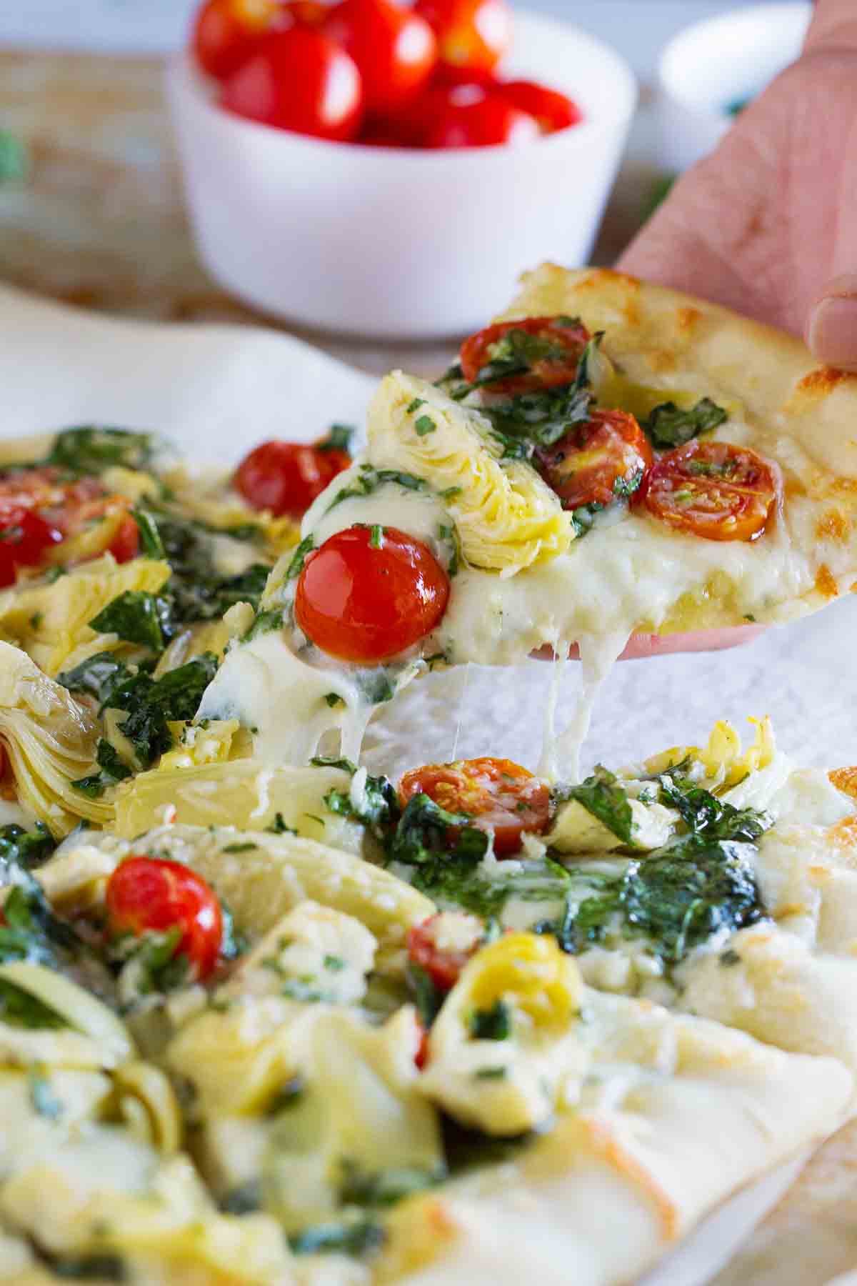 taking a slice of Artichoke, Tomato and Spinach Pizza