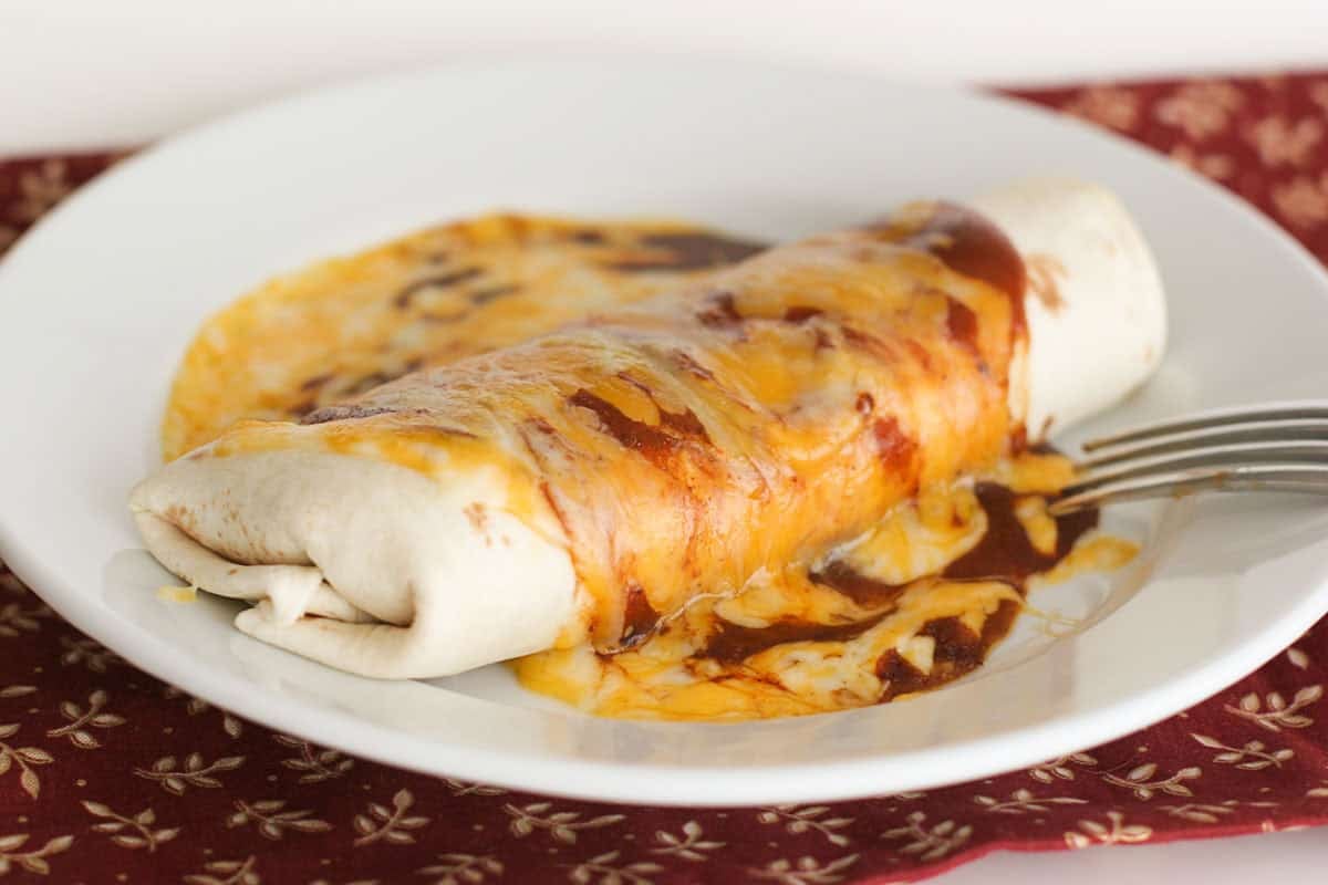 Chili Potato Burrito on a plate, covered in enchilada sauce and cheese.