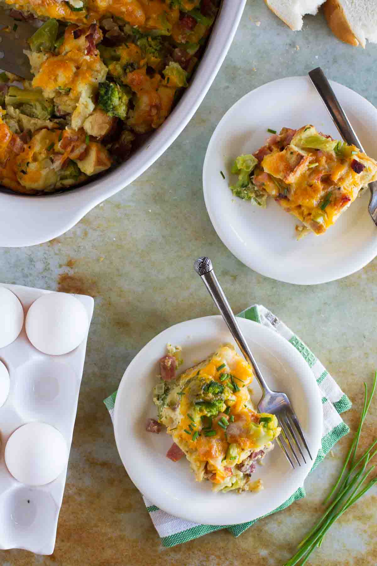 Two servings of ham and cheese strata with the casserole dish close by.