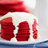 Red Velvet Pancakes on a plate topped with cream cheese icing.