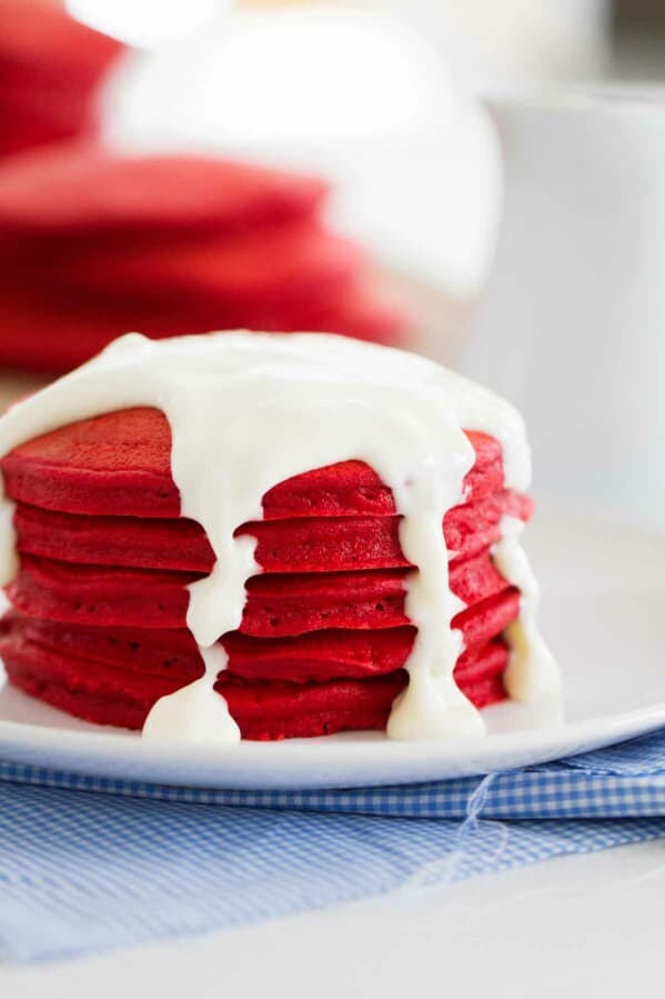 Red Velvet Pancakes on a plate topped with cream cheese icing.