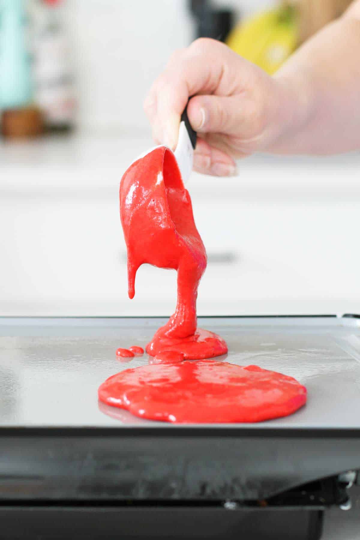 pouring red velvet pancake batter onto a griddle.