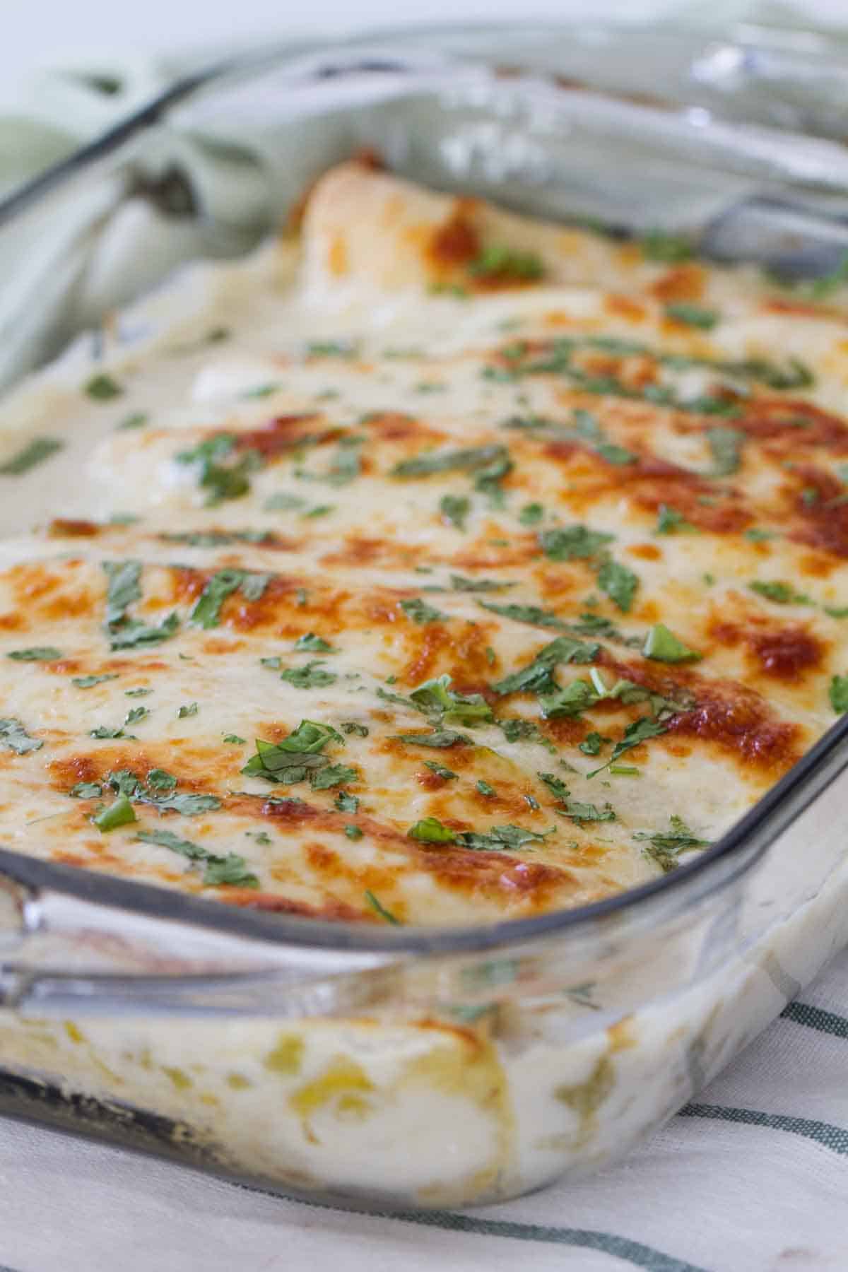 Rich and creamy, these White Chicken Enchiladas are easy chicken enchiladas that are covered in a simple sour cream and green chile sauce. casserole dish with white chicken enchiladas