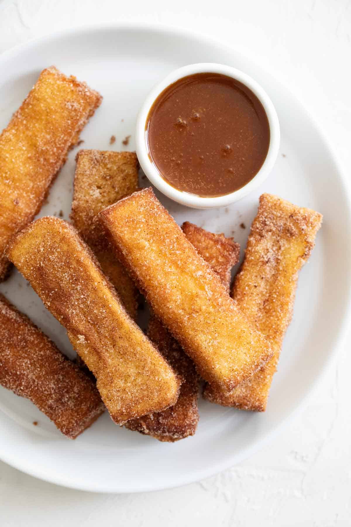 French Toast Sticks on a white plate with a small bowl of buttermilk syrup.