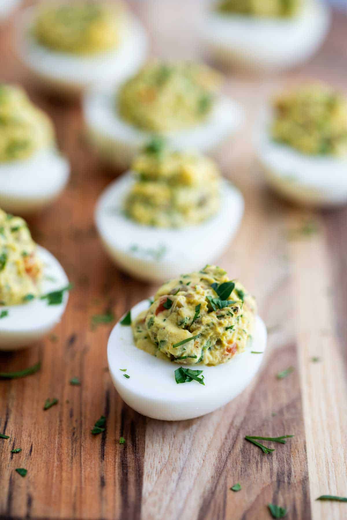 Green Olive Deviled Eggs with Fresh Herbs on a wooden board.