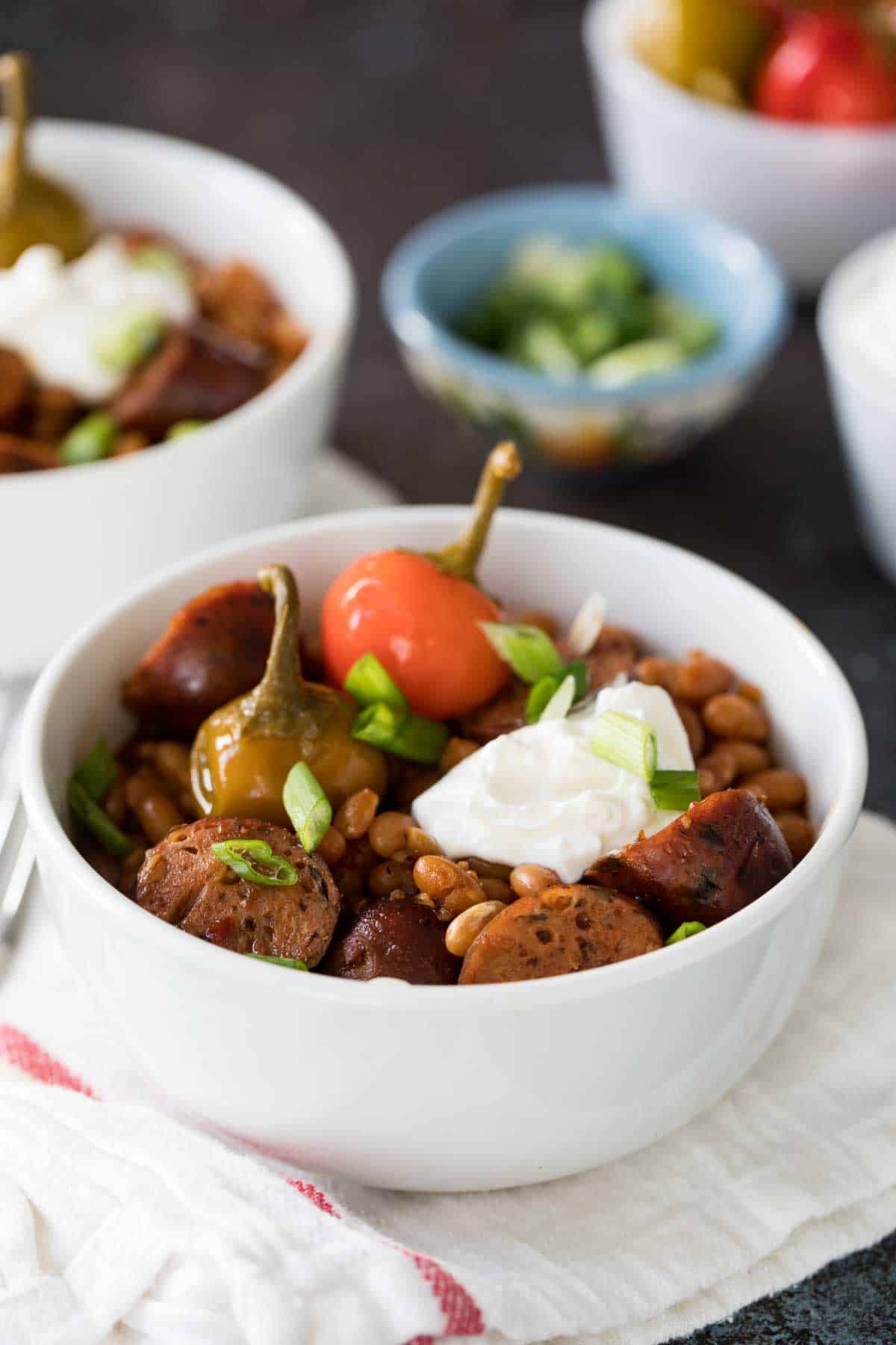 White bowl filled with beans, sausage, sour cream, and peppers.