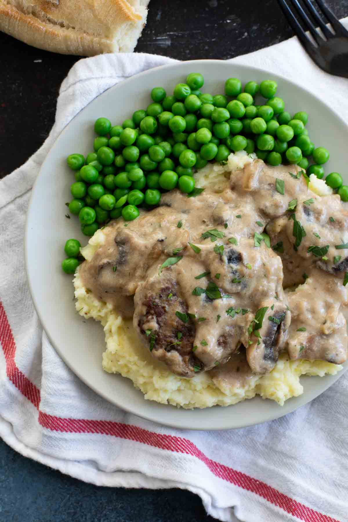 Plate with salisbury steak and gravy over mashed potatoes with peas.