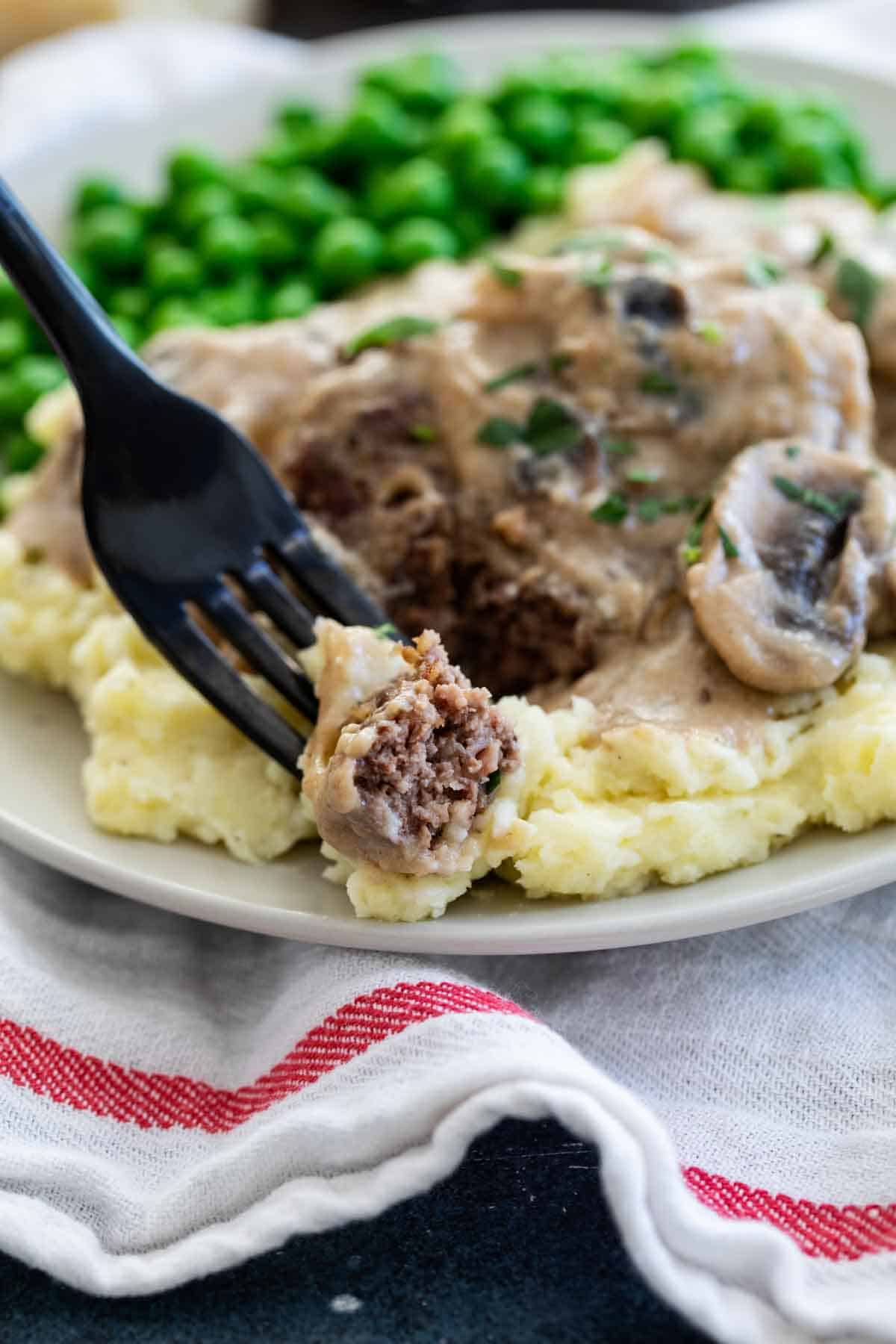 Fork holding a bite of salisbury steak with gravy.