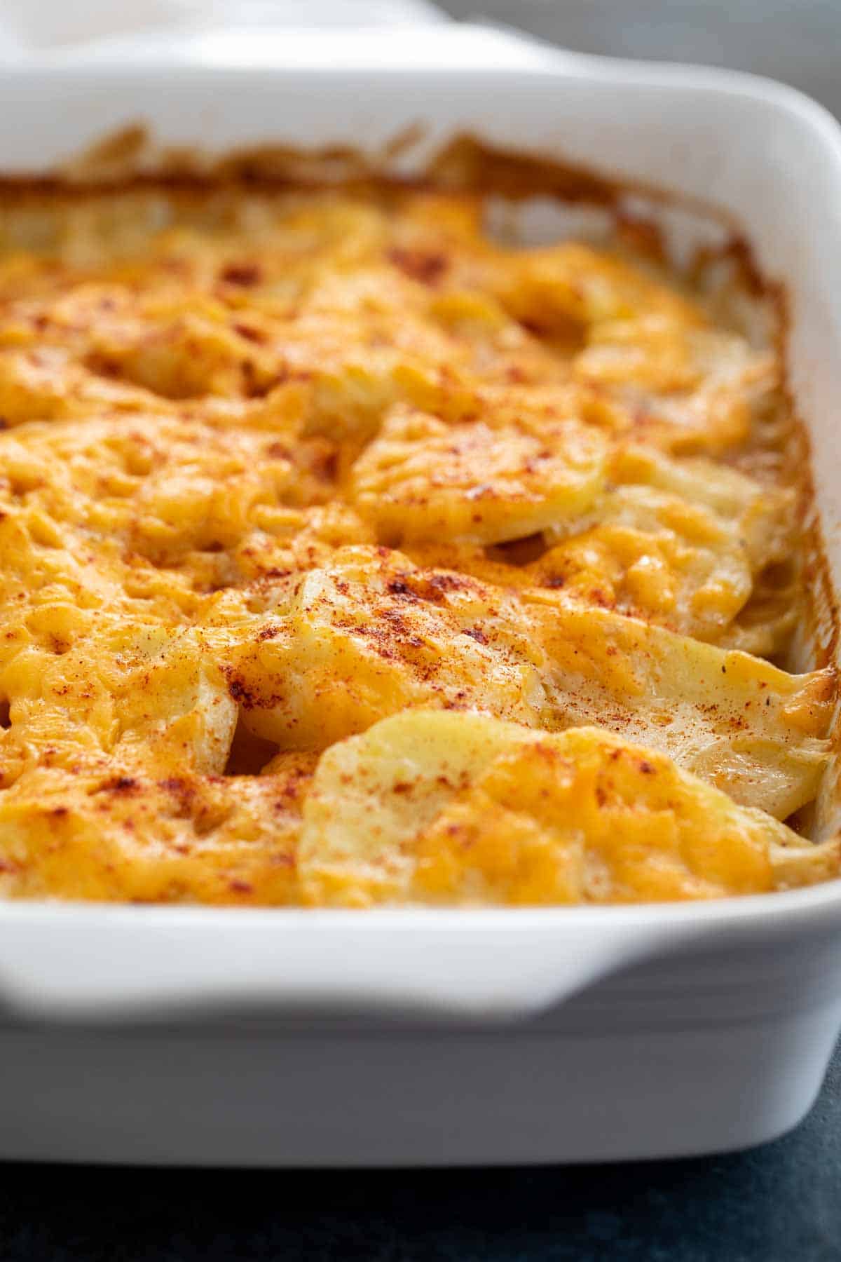 Classic and creamy, this Scalloped Potatoes recipe is a little different because it doesn’t rely on milk, cream or any canned soups. This potato recipe makes the perfect addition to a holiday meal! Scalloped Potatoes in a dish, sprinkled with paprika