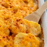 wooden spoon scooping out scalloped potatoes from a baking dish