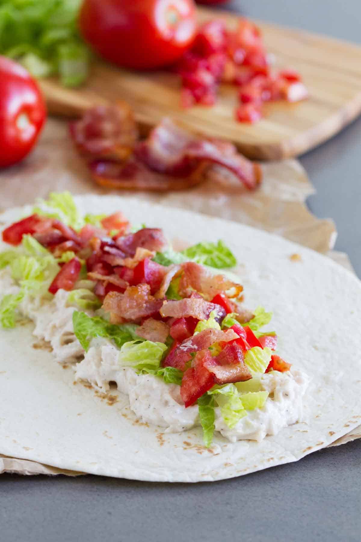 adding ingredients to tortilla for a chicken wrap