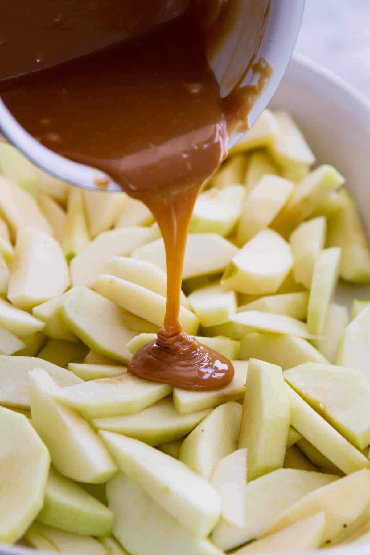 pouring caramel over apples in a baking dish.
