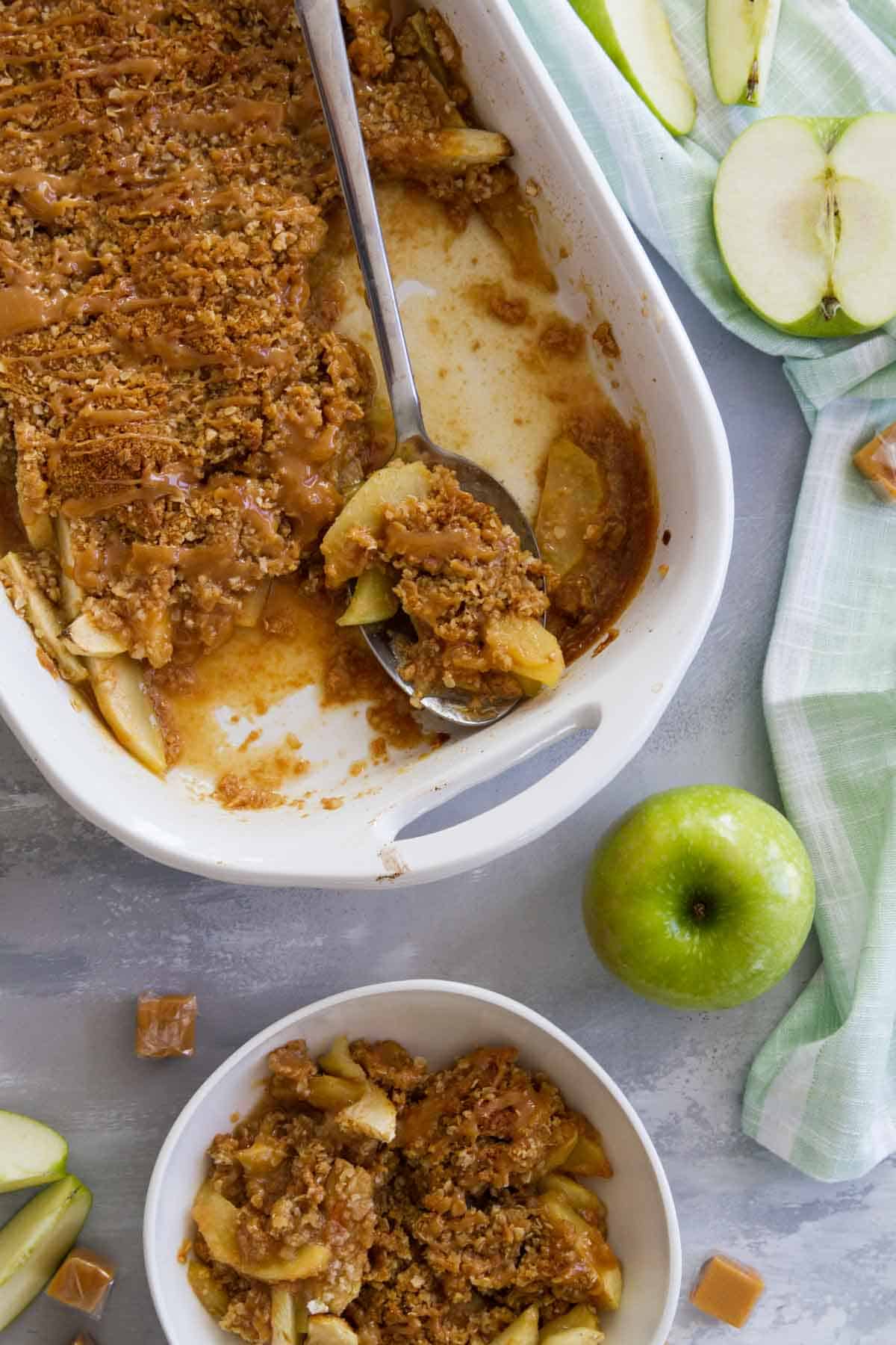 Baking dish of caramel apple crisp with a serving spoon.