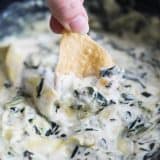 Dipping a chip into the best Crockpot Spinach Artichoke Dip