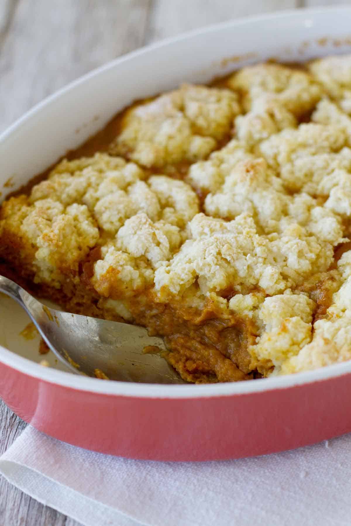 Cobblers aren’t just for summer! A pumpkin custard is covered with a sweet biscuit topping in this fantastic Pumpkin Cobbler. Serve with ice cream for a different holiday dessert. Dish filled with Pumpkin Cobbler - a fall dessert with pumpkin custard topped with a sweet biscuit topping.