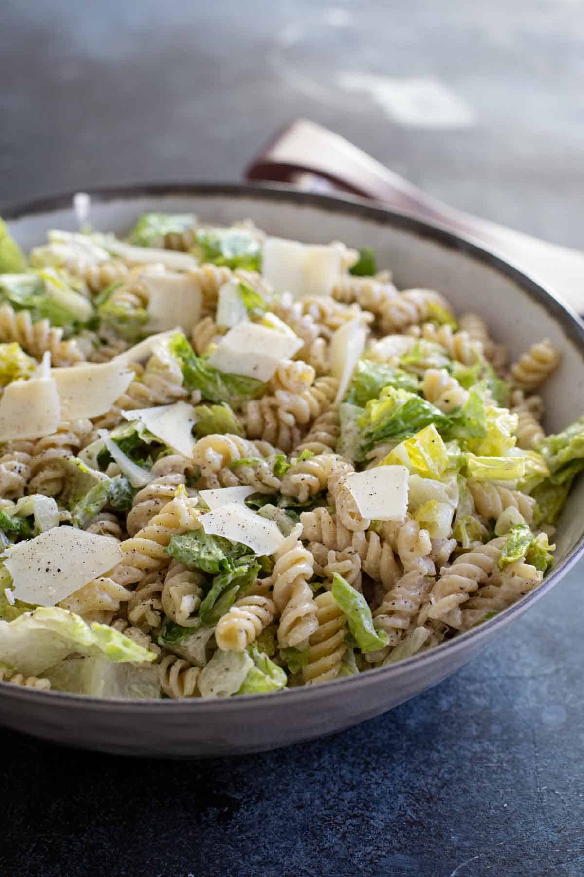 A fresh take on the Caesar salad, this Caesar salad with Pasta is a pasta salad/green salad hybrid that is combined with a homemade dressing for a perfect side dish or potluck salad. Caesar Salad with Pasta with Homemade Caesar Dressing