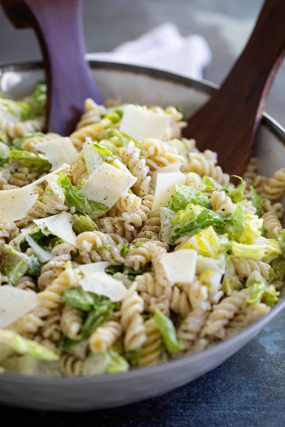 Bowl of Caesar Salad with Pasta with salad tongs.