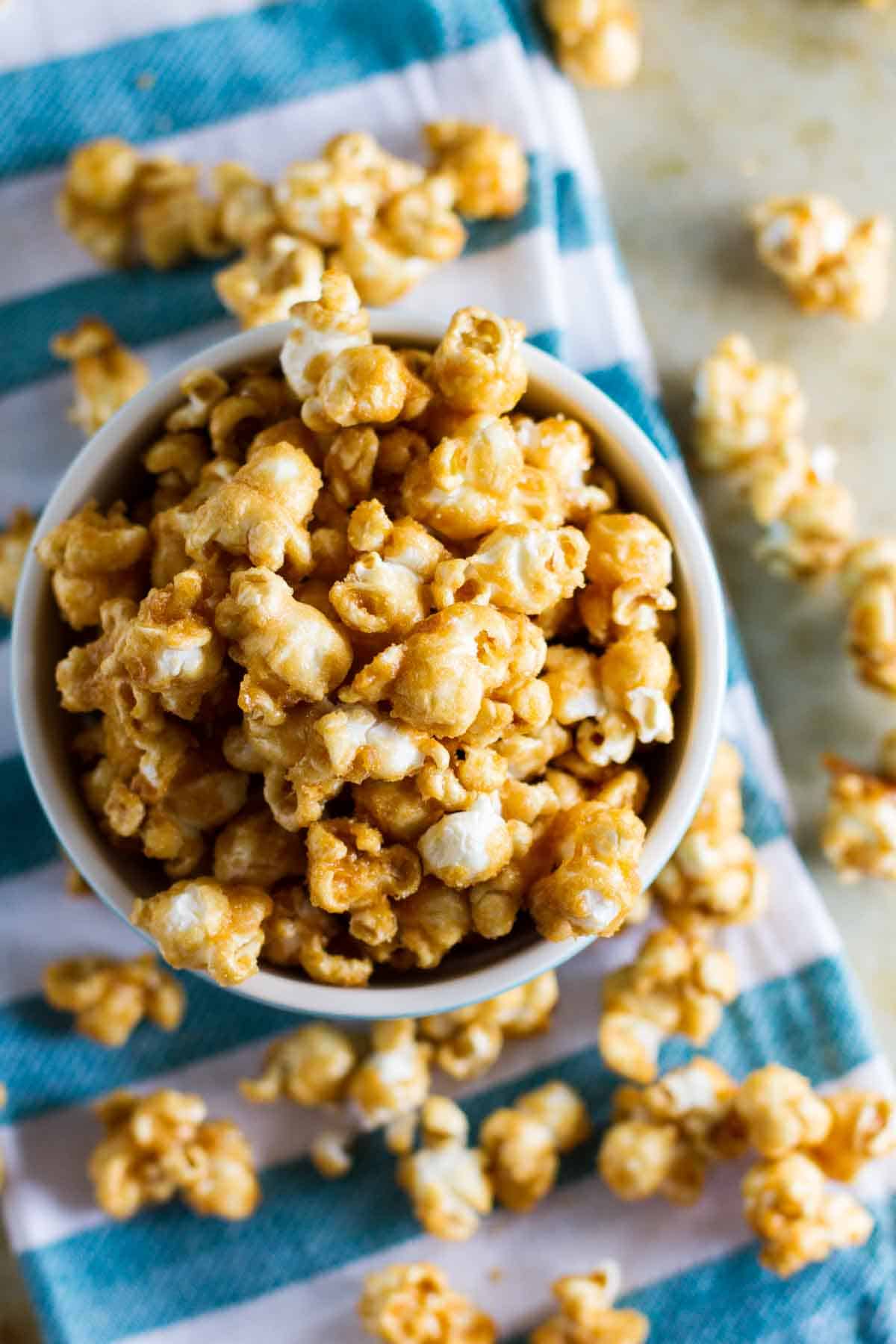 Baked caramel popcorn in a bowl, spilling out to the table below.