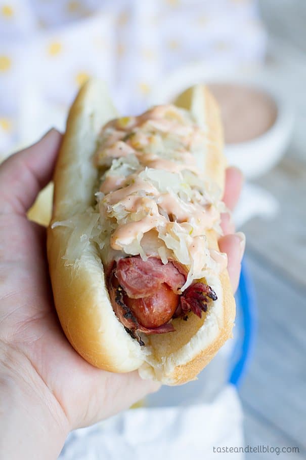 Hand holding a Pastrami Wrapped Hot Dog.