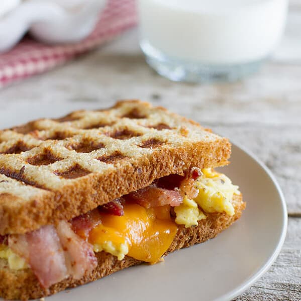 Waffled Breakfast Grilled Cheese Sandwich Recipe - Grilled cheese breakfast style! A breakfast grilled cheese sandwich recipe has scrambled eggs, bacon and cheese on toast that is cooked in a waffle maker for a fun breakfast idea.