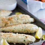 Panko crusted tilapia on a baking sheet with lemons.