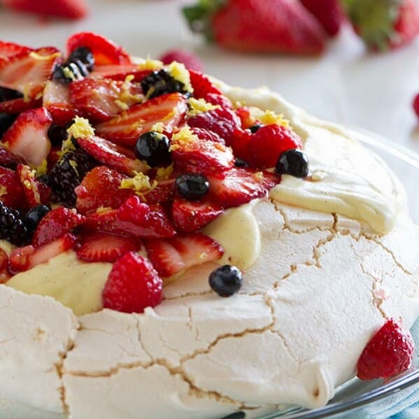 A light and delicate meringue cake is topped with whipped cream, silky creme anglaise and lots of berries in this Pavlova Recipe with Fresh Berries.