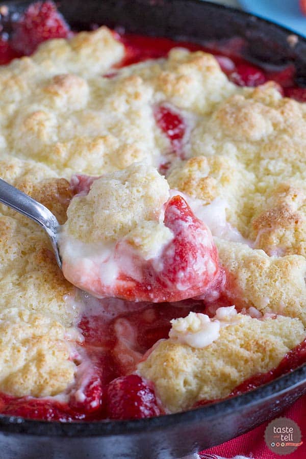 Strawberry cobbler in a cast iron skillet with a serving spoon.