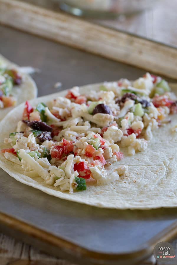 filling for Greek quesadillas on a tortilla on a baking sheet.