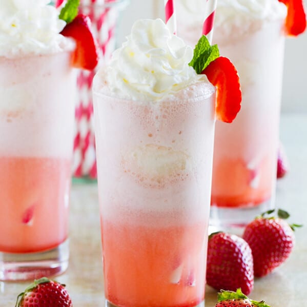 Three strawberry cream floats with fresh strawberries on the side.
