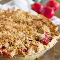 Full strawberry crumble pie, with fresh strawberries in front and behind.