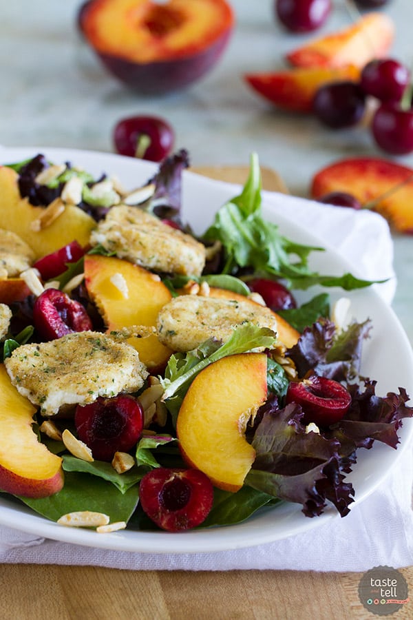 bowl filled with salad topped with stone fruit and fried goat cheese.