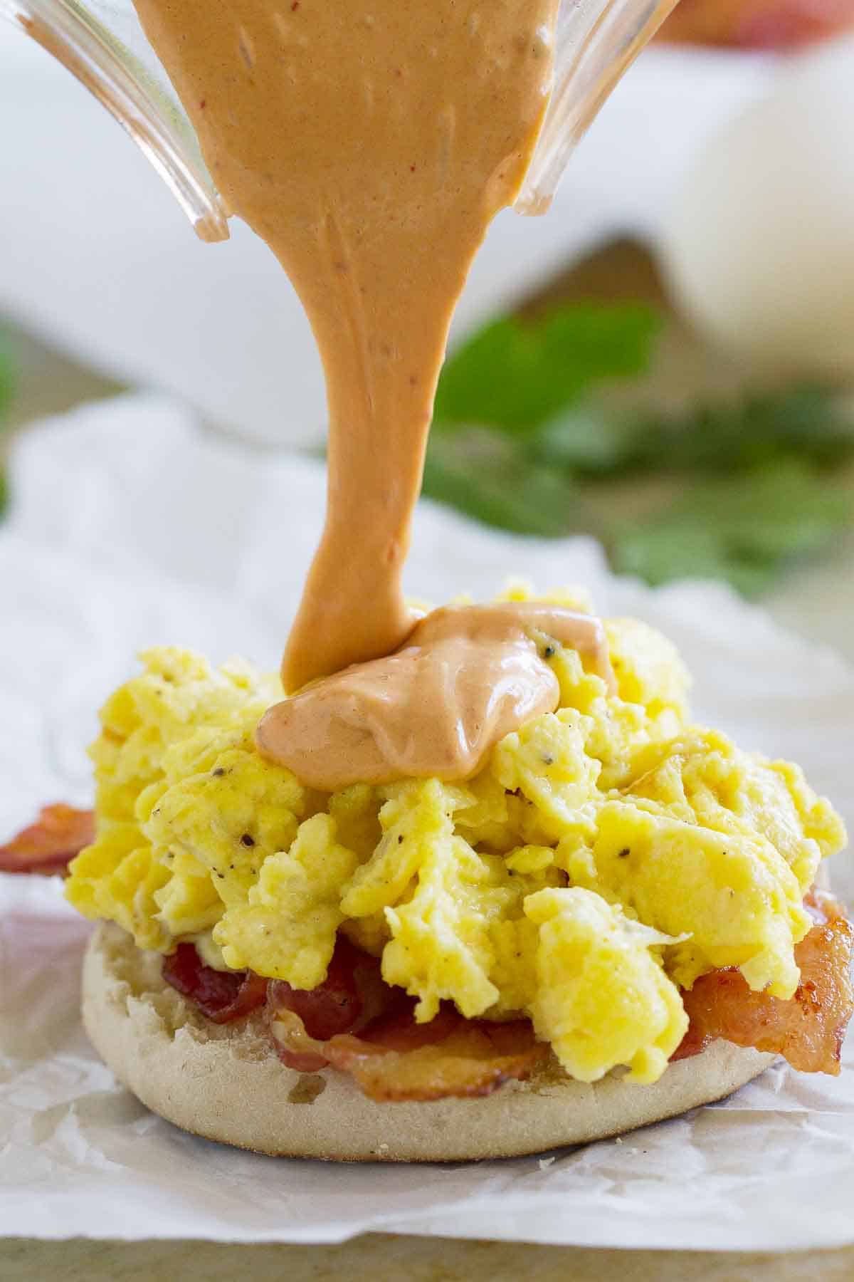 Pouring chipotle hollandaise sauce on top of egg sandwich