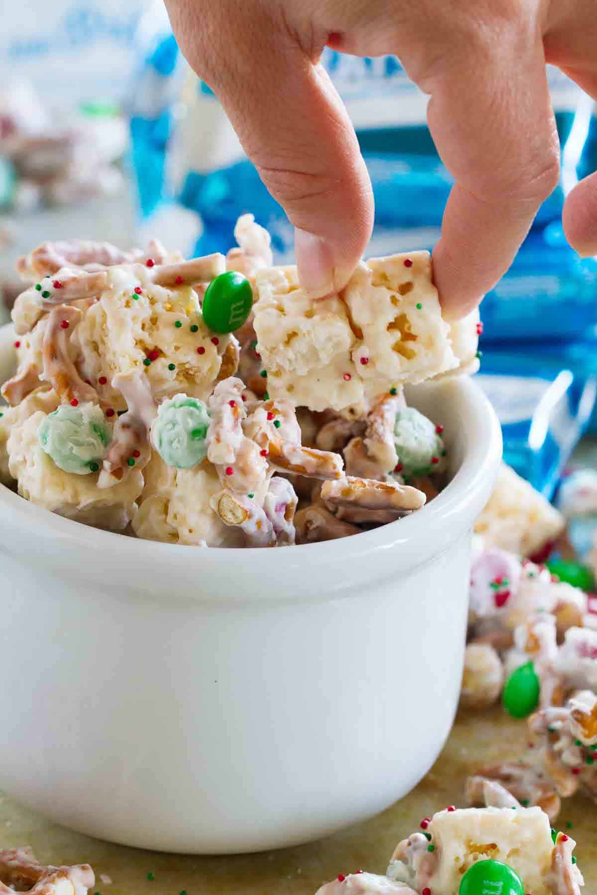 Sweet and salty Christmas mix in a bowl with a hand grabbing some out.