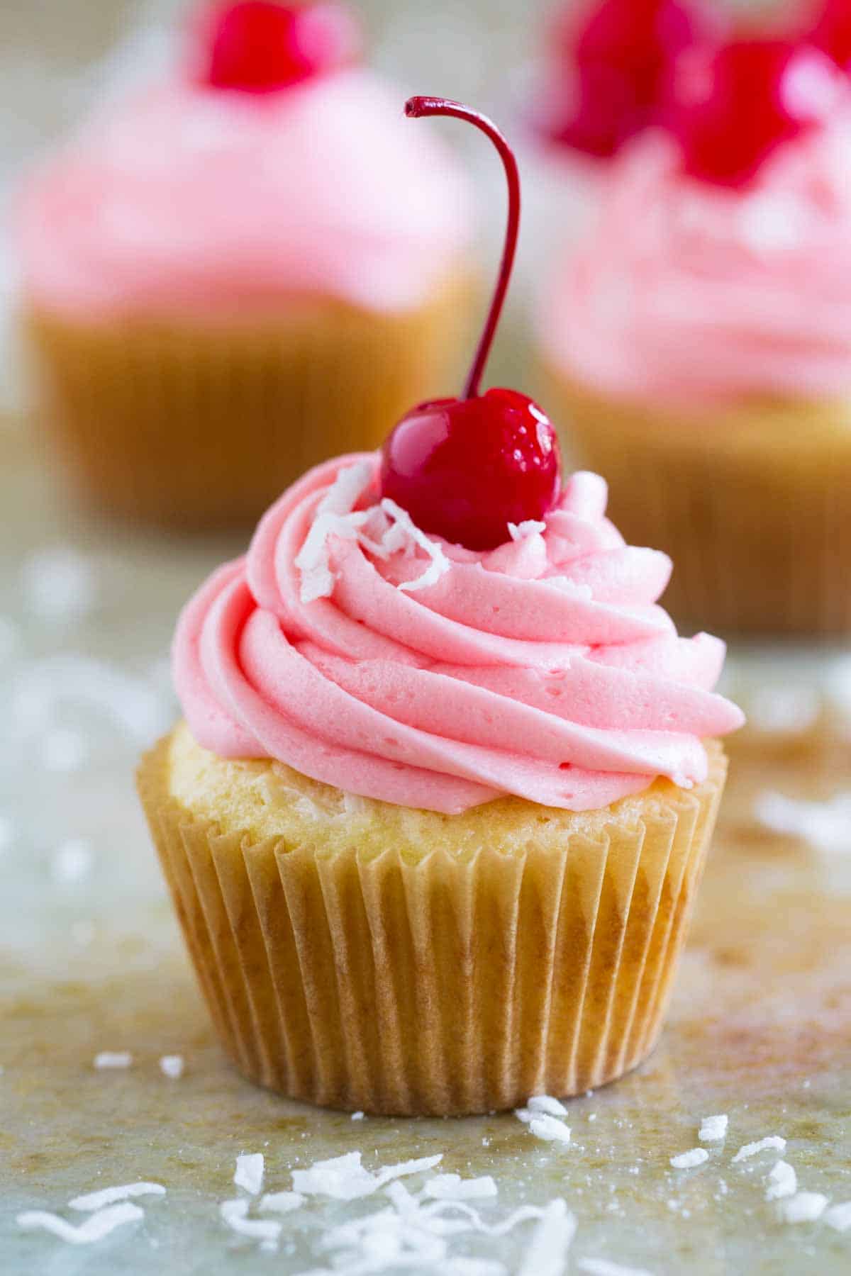 single coconut cupcake with cherry frosting and a cherry on top
