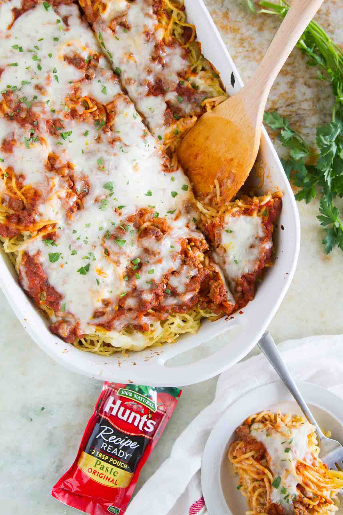 Spaghetti Lasagna in a white baking dish with tomato paste and a plate nearby.