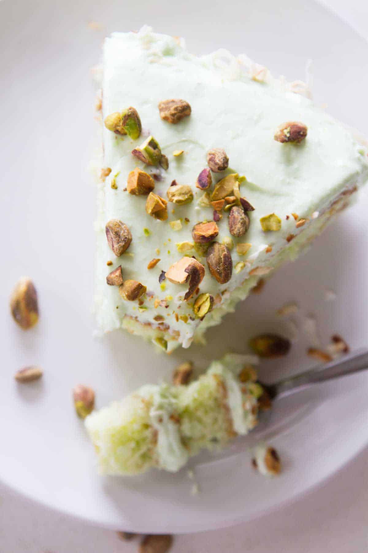 Slice of pistachio pudding cake with a forkful taken from the corner.
