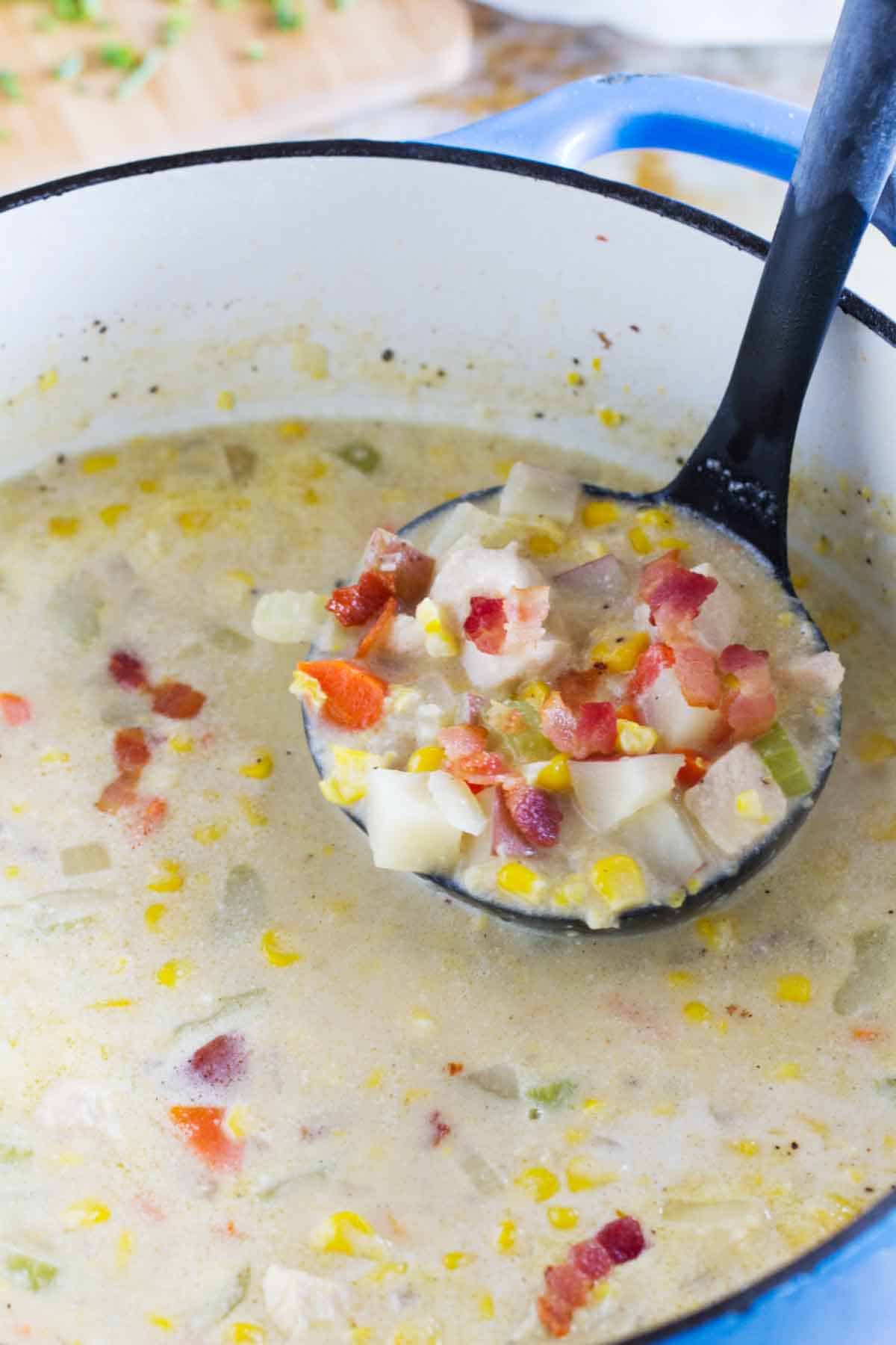 Ladle with a scoop of chicken corn chowder in a dutch oven.