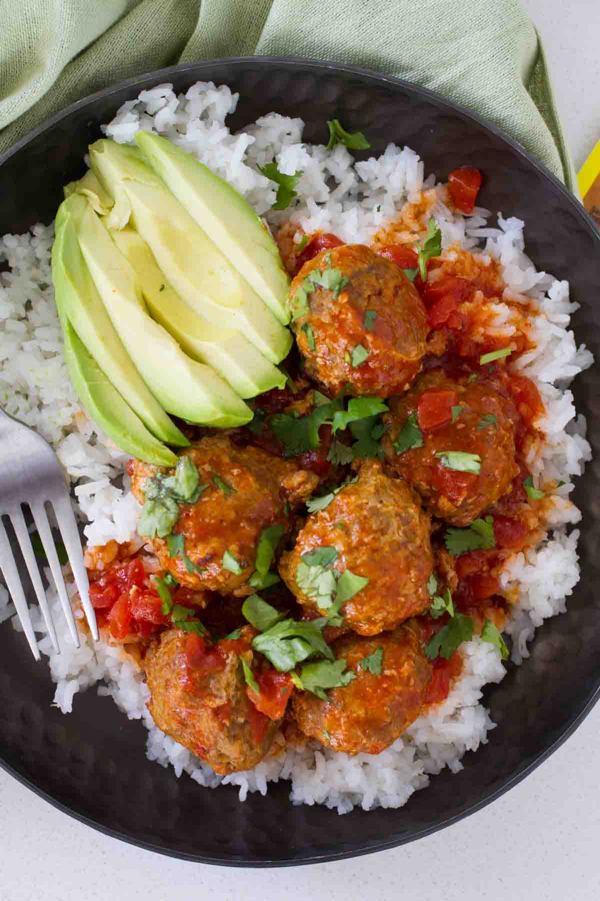 Slow Cooker Mexican Meatballs over rice, with cilantro and a sliced avocado.