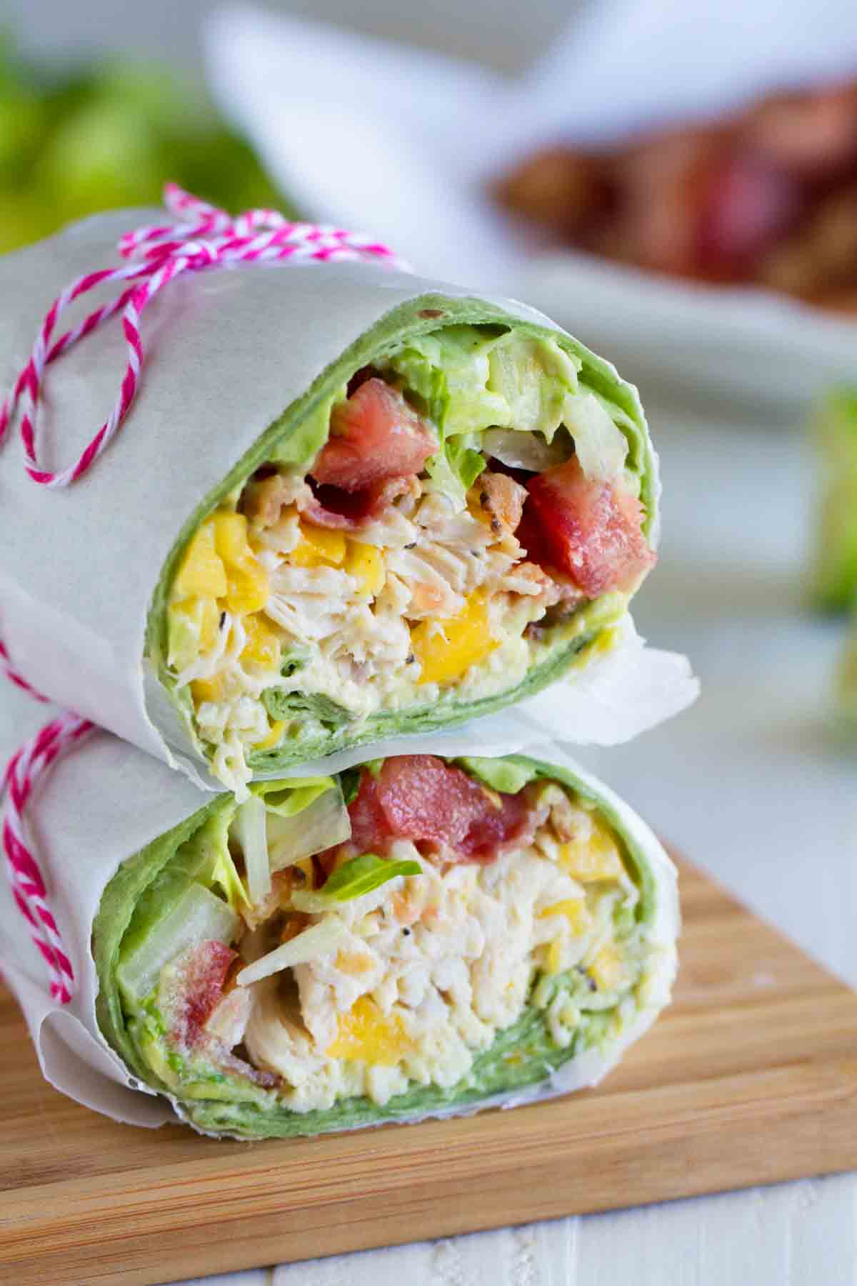 Shredded chicken, mango, avocado and bacon are the stars in this easy California Club Chicken Wrap that is perfect for a weeknight. California Club Chicken Wrap cut in half, halves stacked on top of each other.