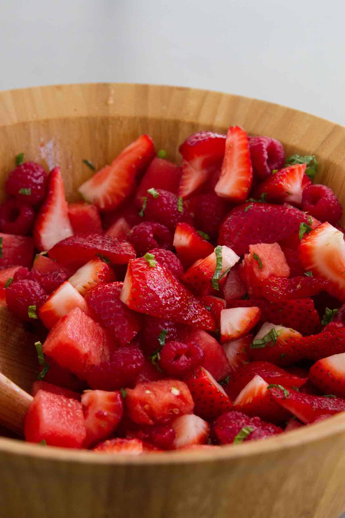 Wooden bowl filled with Crown Ruby Fruit Salad with berries and watermelon.