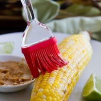 brushing butter on a cob of grilled corn